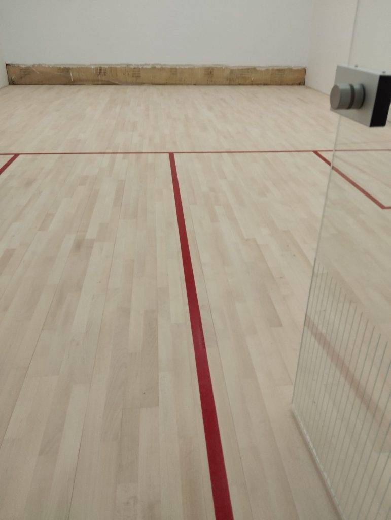 Newly installed squash court with maple wood flooring and red boundary lines.