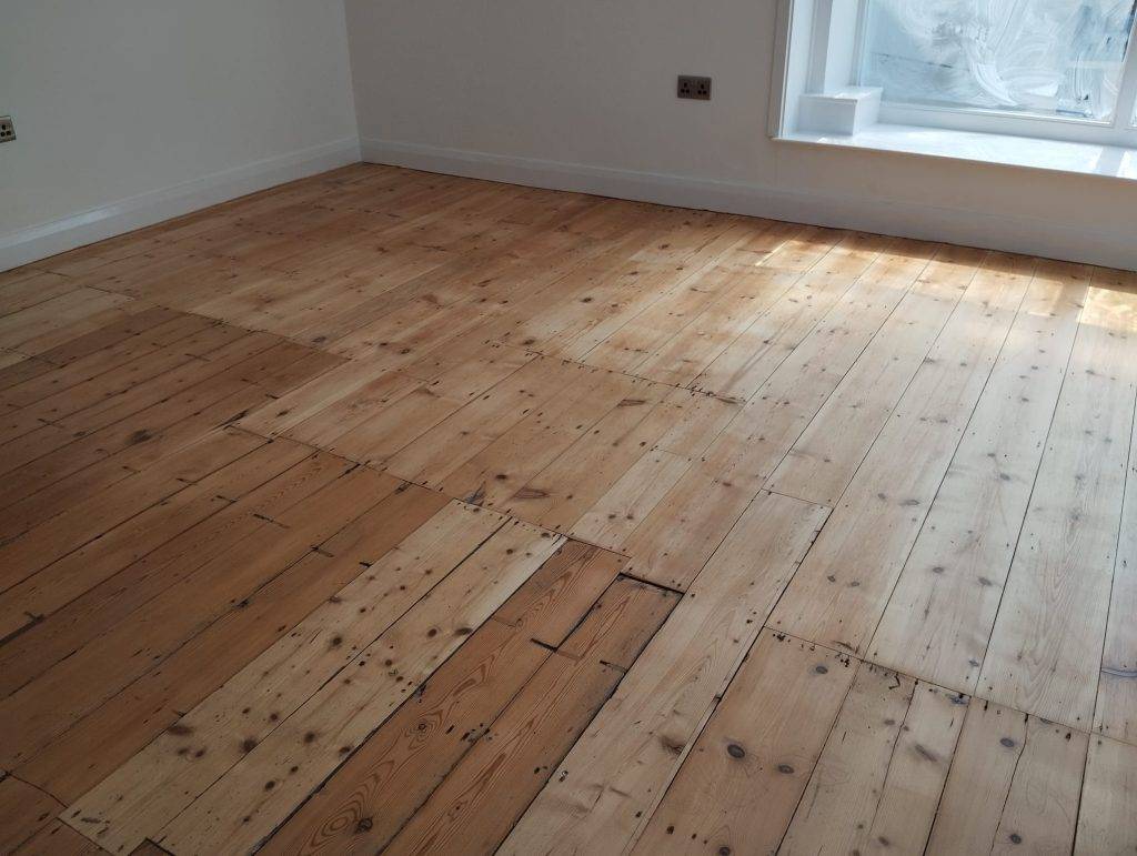 Restored pine wood flooring in sunlit room with white walls