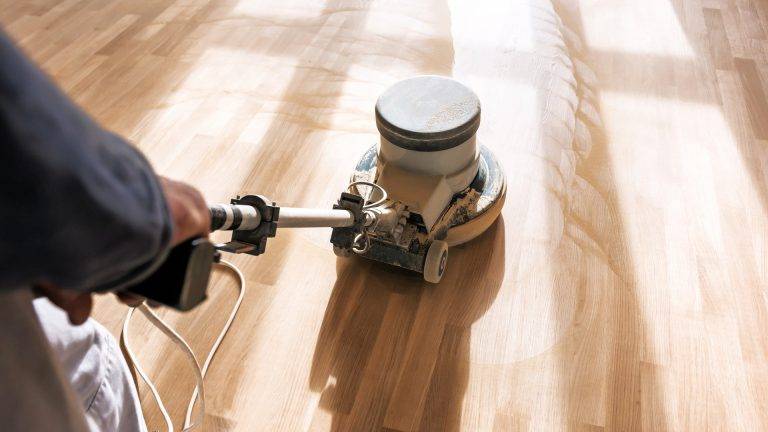 Person polishing a wooden floor with an industrial floor polishing machine.